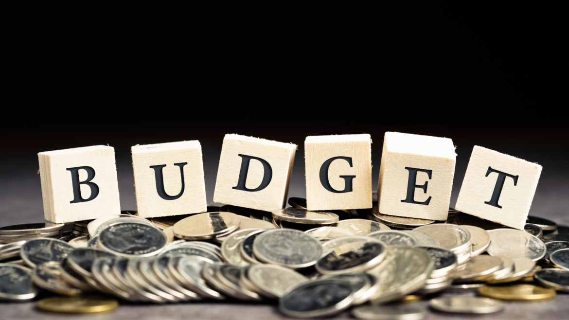 The word 'Budget' spelled out using blocks, resting on a bed of gold coins.